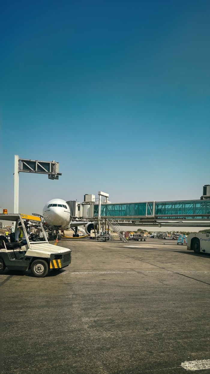 Home Aircraft parked at Karachi airport apron connected to terminal bridge on a clear day.