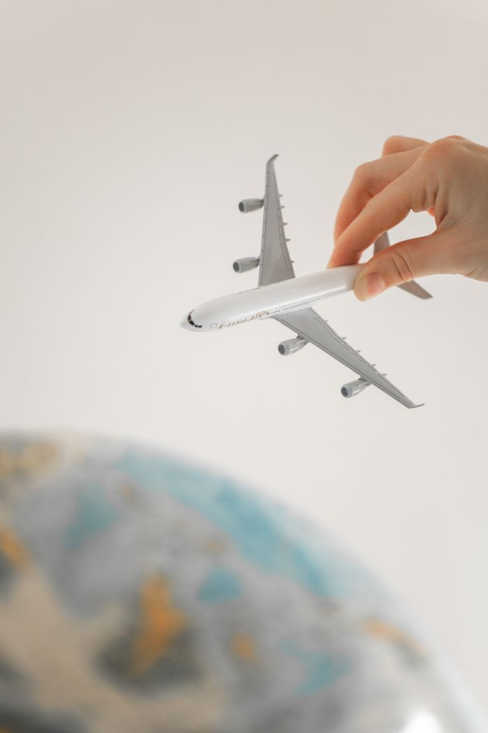 Home Close-up of a hand holding a toy airplane over a blurred globe, representing travel planning and adventure.